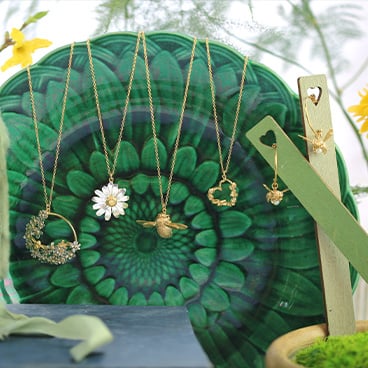 Alex Monroe Jewellery bee and daisy mix of necklaces placed info of a green plate