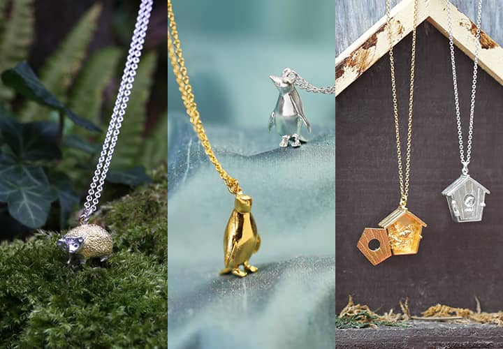 Hedgehog Necklace in a mossy surrounding, 2 Adelie Penguin Necklaces on flowing blue fabric and 2 Birdhouse Lockets hanging from a decorative wooden house.